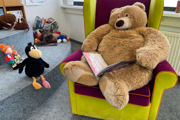 Teddybär sitzt im Sessel mit Buch auf dem Schoß