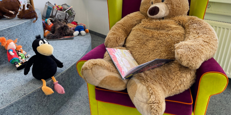 Teddybär sitzt im Sessel mit Buch auf dem Schoß