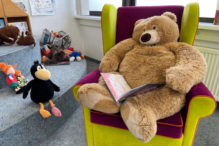 Teddybär sitzt im Sessel mit Buch auf dem Schoß