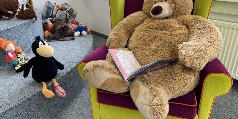 Teddybär sitzt in Sessel und liest vor