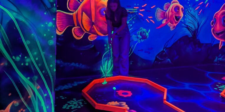 Ein blauses Bild mit einer rotumrandeten Minigolfbahn und angedeuteten Pflanzen und roten Fischen in einem Aquarium