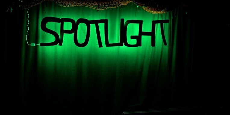 Schwarzer Schriftzug SPOTLIGHT auf grünen leuchtenden Hintergrund