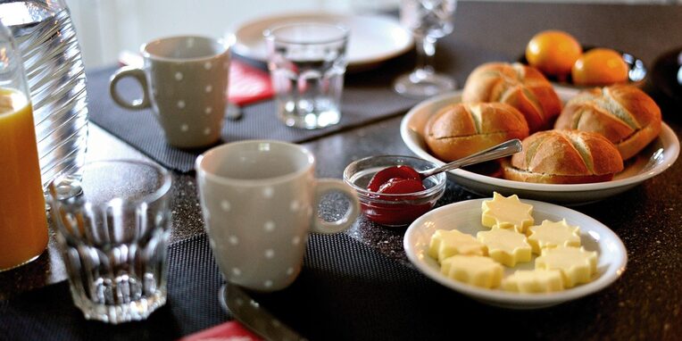 Ein gedeckter Frühstückstisch mit Brötchen, Butter und Marmelade