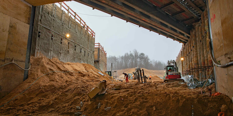 Tunneldurchstich Regionaltangente West am Kreuzungsbauwerk Neu-Isenburg, Blick aus dem Tunnel mit Sandhügeln, Baugeräten und Arbeitern