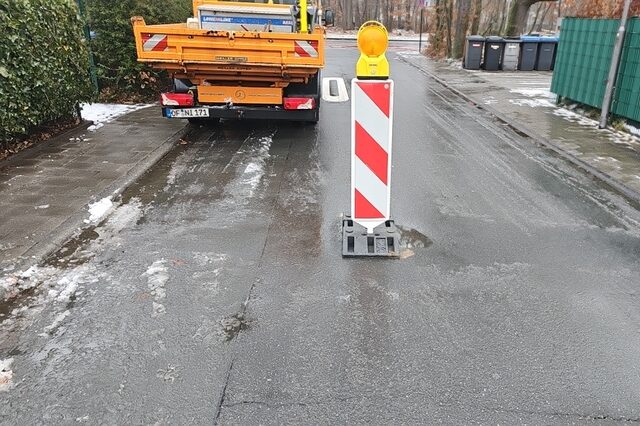 Warnbarke in der Straßenmitte am linken Bildrand steht ein orangefarbenes DLB Fahrzeug