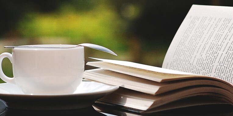 Eine weiße Tasse mit Unterteller und Kaffeelöffel und einem aufgeschlagenen Buch