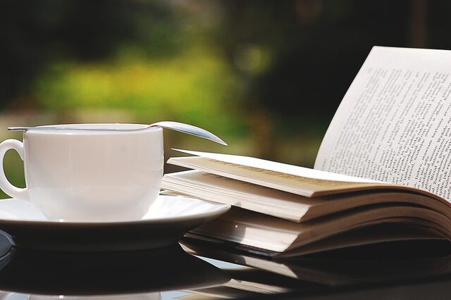 Eine weiße Tasse mit Unterteller und Kaffeelöffel und einem aufgeschlagenen Buch