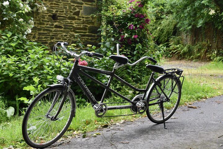 Ein schwarzes Tandem-Fahrrad auf einem Waldweg vor einer Steinmauer
