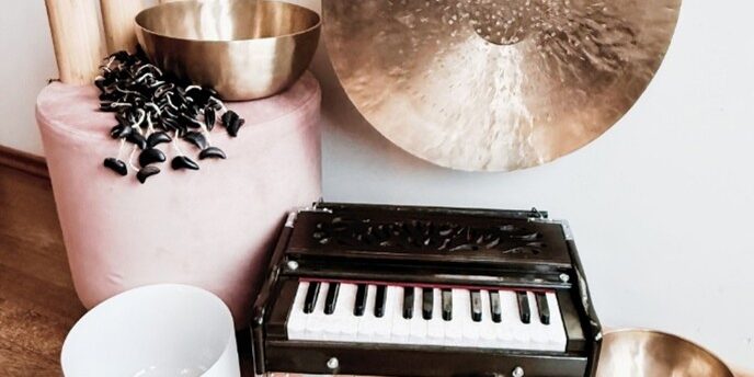 verschiedene Klangschalen, ein Gong, ein kleines Minipiaano präsentieren sich auf einem braunen Holzboden