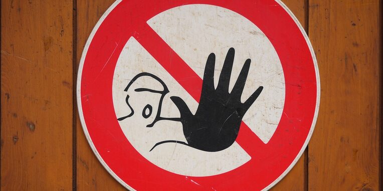 rundes rot weißes Warnschild mit einem Gesicht und einer Hand